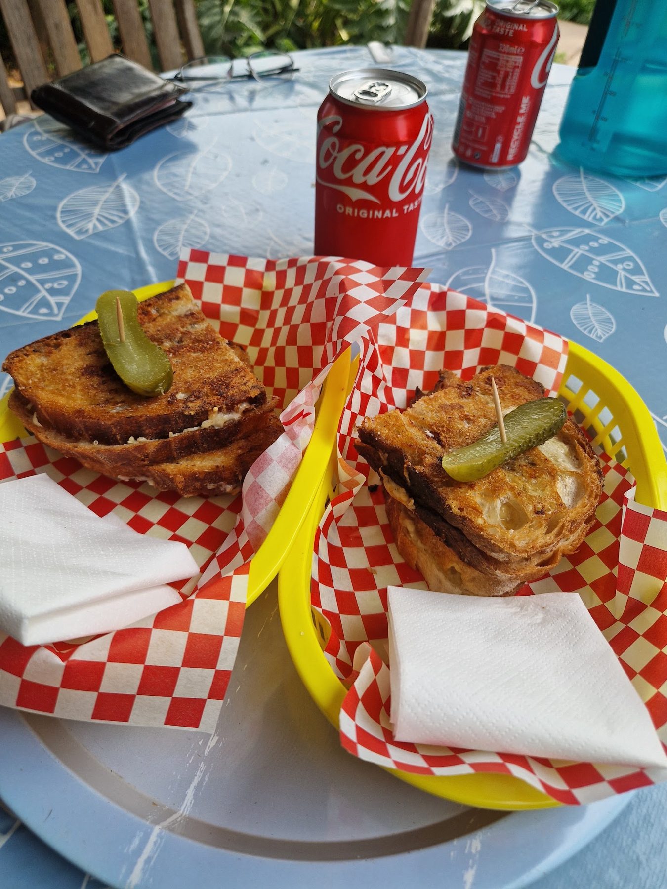 Two grilled cheese toasties with pickles on a table by the river